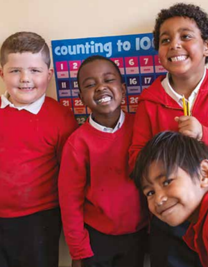 Four schoolchildren in red jumpers smile at the camera